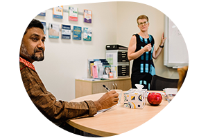 Man and woman sitting apart looking at each other as mediator stands behind taking notes